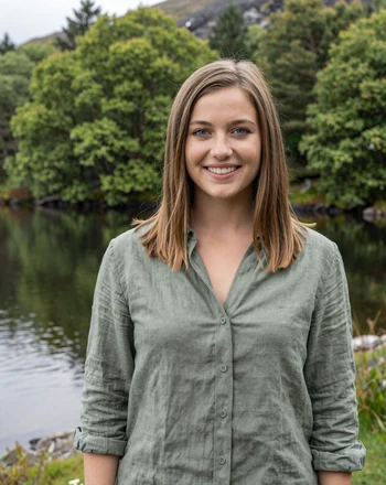 Orla, 24, Irish woman from Killarney standing in Killarney National Park with lush green trees and a glassy lake