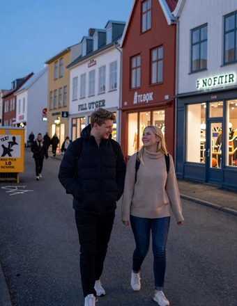 Couple walking along Laugavegur street in Reykjavik at dusk with colorful shops and street art