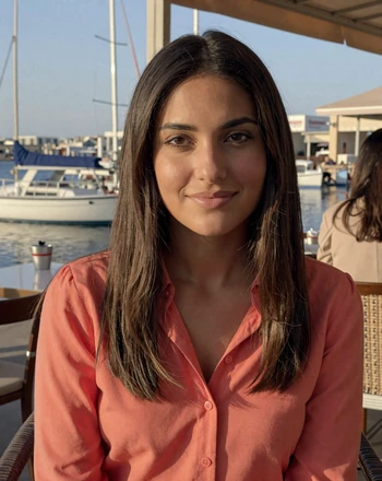 Elena, 27, Cypriot woman from Limassol sitting at a seaside cafe with marina boats in the background