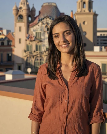 Elena, 33, Spanish woman from Barcelona smiling on a rooftop with Gaudi architecture behind her